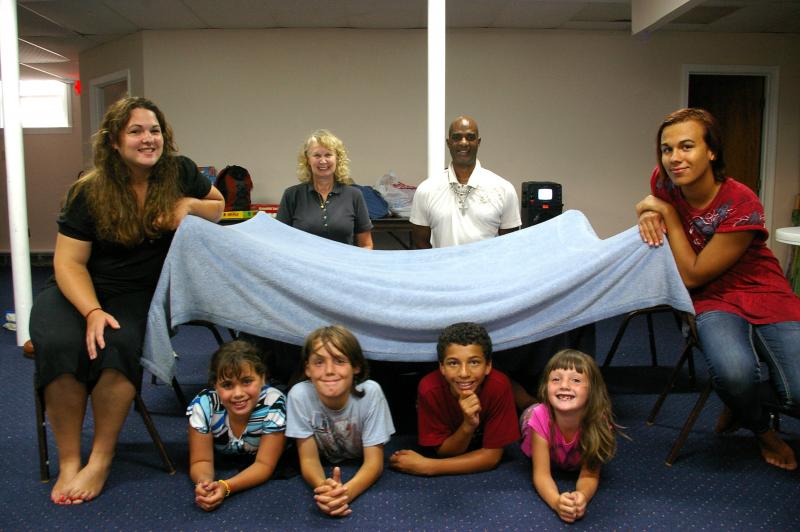"30 Hour Famine" participants hang out next to their makeshift tent in the basement of the Emmanuel Assembly of God in Onset. Front row, from left to right, Youth Director Tabitha Kelley, 10-year-old Cheyenne King, 12-year-old Ryan Hulslander, 12-year-old Jaylen Gore, 6-year-old Fiona Butterfield, and Assistant Youth Director Tyrone Cabral. Back row, Children's Bible Class Teachers Joan Guenard and Gregg Johnson. BY RISHI SIDHU